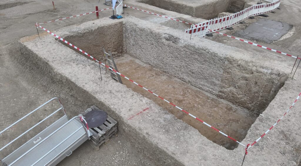 Baugrube, die Abgesperrt ist mit Flatterband. Es gibt an dem linken Rand eine Leiter zum Einstieg.